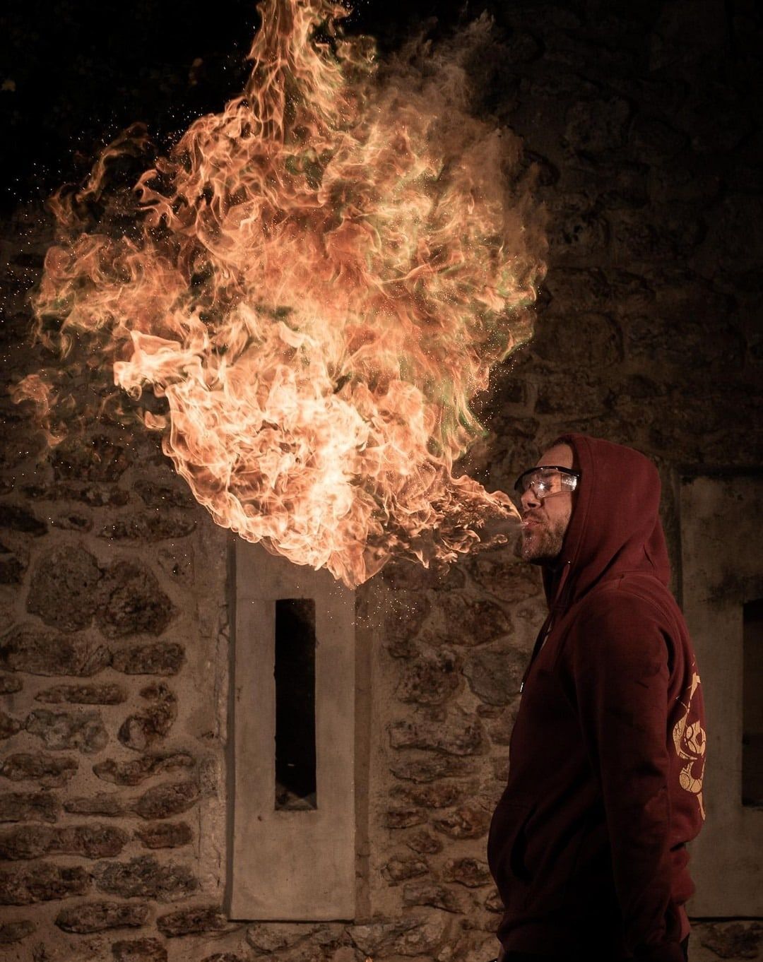 Flamme rosée contre un mur de pierre, le cracheur en capuche