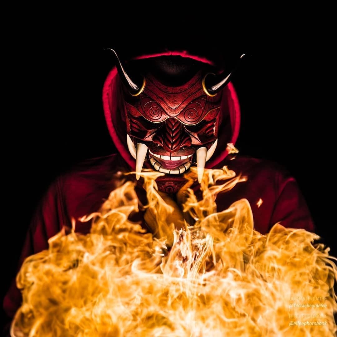 Masque de démon rouge émergeant d’un mur de flammes